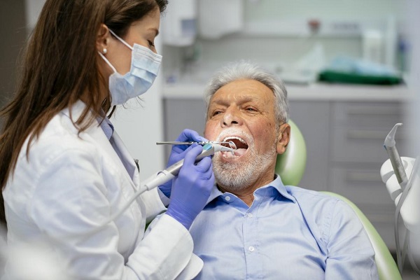 A lady dentist is examining the dental health of an old man with the help of dental probe and mouth mirror.